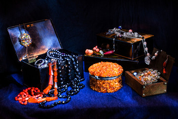 Vintage old wooden caskets with jewelry,  coral and amber necklaces. Amber box in the center. Light brush shooting. Dark background.