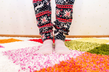 Women's legs in pajamas and socks on the bright carpet.