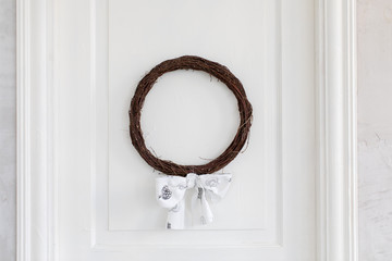 Decorative wreath made of small twigs adorned with white tied bow.