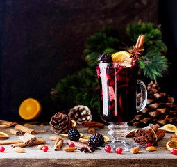 glass of hot mulled wine for the new year with ingredients for cooking, nuts and Christmas decorations