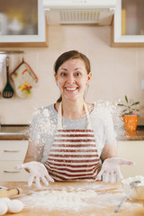 A young funny cheerful woman sitting at a table with flour and going to prepare a Christmas cakes in the kitchen. Cooking home. Prepare food.