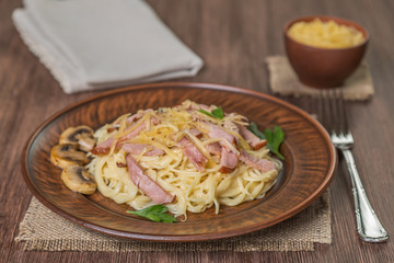  Pasta Carbonara with bacon and mushrooms in ceramic dishes on the table made of oak planks. Brown. 