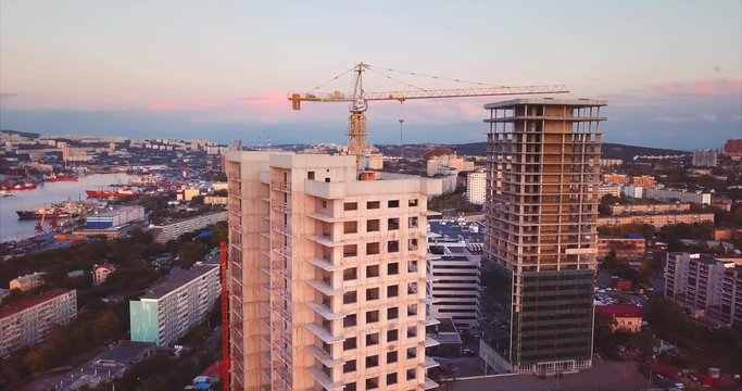 Aerial panoramic view of new high buildings under construction in Vladivostok. Peter the Great Gulf in the Sea of Japan with moored ships is on the background. Sunset. Russia