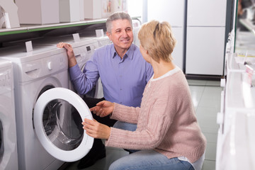 friendly mature couple chooses washing machine for their house in shop of household appliances