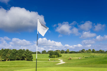View of a green golf course, hole and flag on a bright sunny day. Sport, relax, recreation and leisure concept. Summer landscape with sunbeams