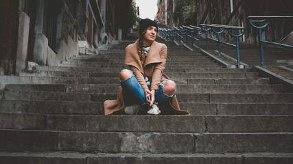 Outdoor lifestyle portrait of a beautiful Caucasian female sitting on a stairway with her phone in hands. Horizontal orientation