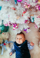 Little boy in blue suit lies among pink toys on the floor