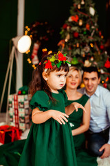 Litle girl in green dress walks before a Christmas tree in the room