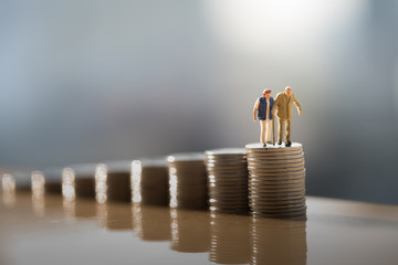 Concept of retirement planning. Miniature people: Old couple figure standing on top of coin stack. - obrazy, fototapety, plakaty