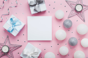 Empty paper blank, gift box and decoration on pink table top view. Christmas mockup or greeting card. Flat lay.