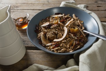 Bowl of breakfast cereal, honey and milk on wooden table