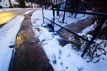 An icy sidewalk passes over a small creek in a snowy environment.