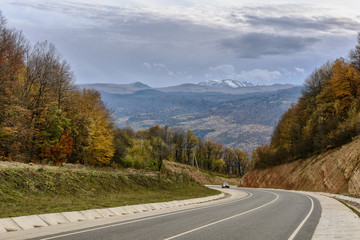 The car travels along the highway among the autumn forest in the mountains of Krasnodar Territory in Russia