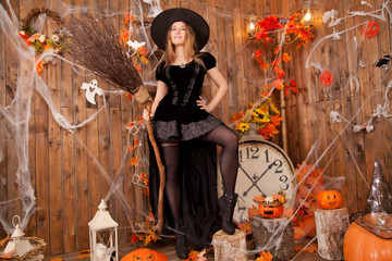 Naklejka premium beautiful classic witch woman wearing black sorceress velvet dress and pointed hat, with orange evil halloween pumpkins and spiderweb 