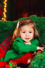 Charming little girl sits in soft armchair before a Christmas tree