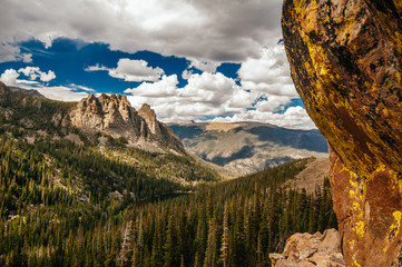 Mountain and lake viewed from behind a moss-covered boulder on a hiking trail in the Rocky Mountains.
