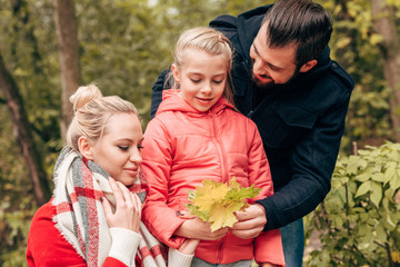 family holding autumn leaves in park