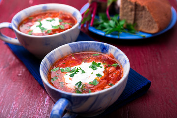 Ukrainian traditional borsch. Russian vegetarian red soup  in blue bowl on red wooden background.  Borscht, borshch with beet. Two plates. Close up.