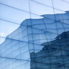 part of geometrically shaped modern glass building with reflections of blue sky and glass wall