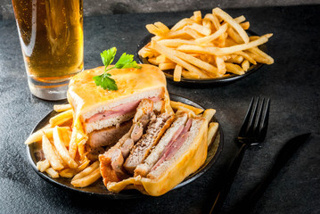 Traditional Portuguese snack food. Francesinha sandwich of bread, cheese, pork, ham, sausages, with tomato beer sauce and French fries. With a glass of beer and potatoes. On black table. Copy space