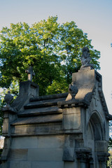 Obraz premium graves against gray richly carved and decorated tombstone surrounded by greenery and warm sunshine shining from behind the trees