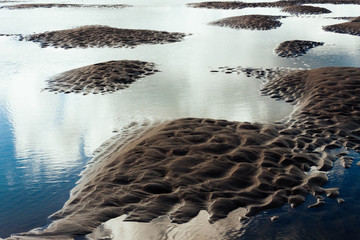Clouds are reflected in shallow tidal pools at De Haan, Belgium.