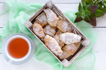 Homemade croissants with jam, decorated with powdered sugar and a cup of morning tea on a white wooden background. Top view.
