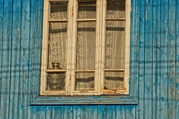 старое окно с занавеской на синей деревянной стене