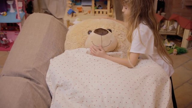 A cute little girl giving the goodnight kiss to her toy friend, a giant teddybear, and hugging him.
