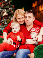 Fototapeta na wymiar Family with two sons dressed in red poses before a green Christmas tree