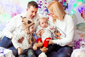 Mom and dad sit with thier two little sons in a pink room with Christmas tree