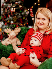 Mom sits with a son in a soft armchair before Christmas tree