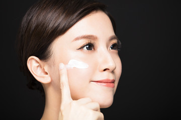 young woman applying lotion cream on face.
