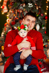Dad holds little daughter in red dress posing before a Christmas tree
