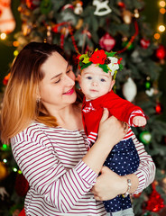 Charming woman holds her little daughter posing before a Christmas tree