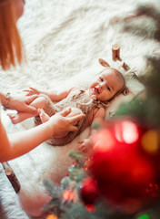 Charming little girl lies on soft beige pillow under a Christmas tree while mother plays with her