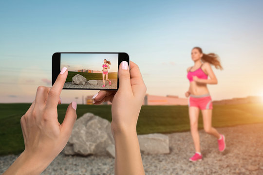 Closely image of female hands holding mobile phone with photo camera mode on the screen. Cropped image of running woman. Runner jogging in sunny nature.