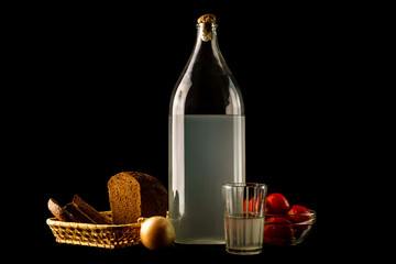 Naklejka premium Ukrainian national drink and snack. The big bottle and glass of moonshine and snack isolated on black background
