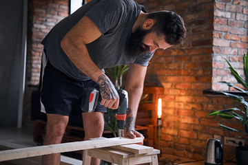 Carpenter drilling a hole in a board in a room with loft interio