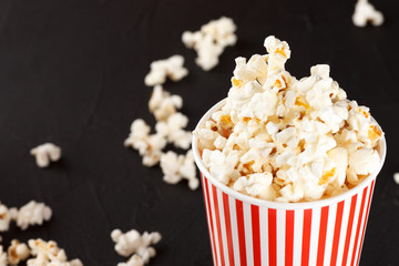 Popcorn horizontal banner. Red stripped paper cup and kernels lying on dark background. Copy space.