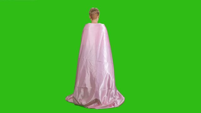 Pretty girl in pink satin bedsheet poses for camera at green background