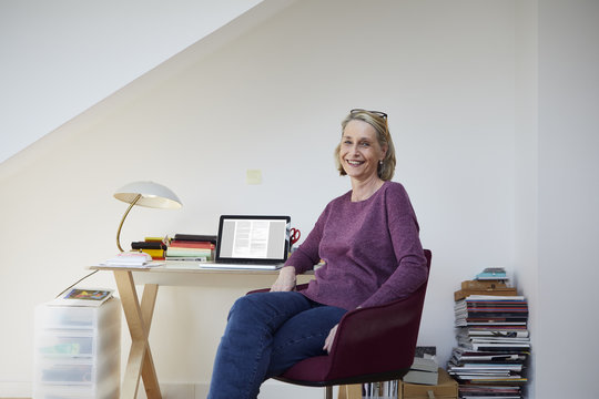 Portrait of smiling mature woman at home with laptop at desk