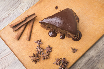 A piece of chocolate cake, cinnamon sticks and anise star on a wooden background