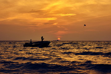 Silhouette of man in boat and parachute in sky against the golden sunset.