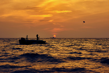 Silhouette of man in boat and parachute in sky against the golden sunset.