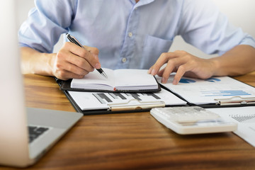 business men working on wooden desk(table) with notebook computer paper, pencil and hand in office, financial concept.