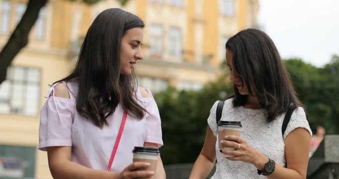Two sisters chatting and drinking coffee outdoors. They are having a lively conversation.
