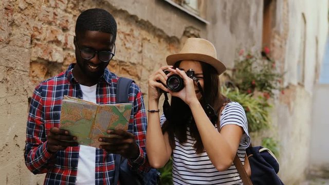 Two young attractive tourists looking on city map in old street of town on holidays. Outdoors. Smiling. Multi-ethnic.