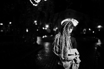 Obraz na płótnie Canvas Girl with dreadlocks walking at night street of city against garland lights.