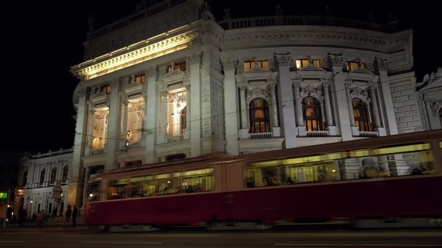 Static low angle night shot of tram arriving at stop in front of Burgtheater in Vienna